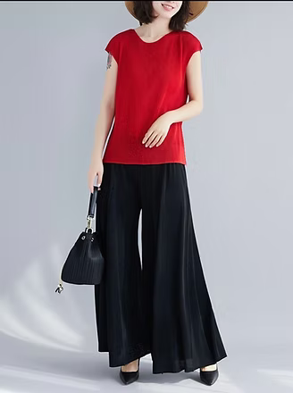 Woman wearing a red top and black pants holding a black handbag on a gray background