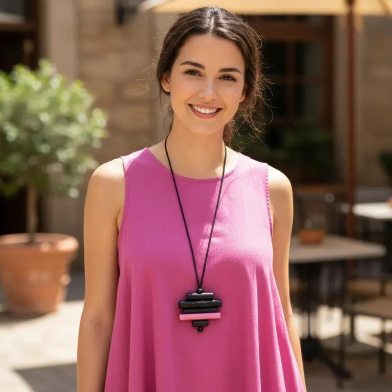 Woman wearing a pink dress with a black necklace in an outdoor setting