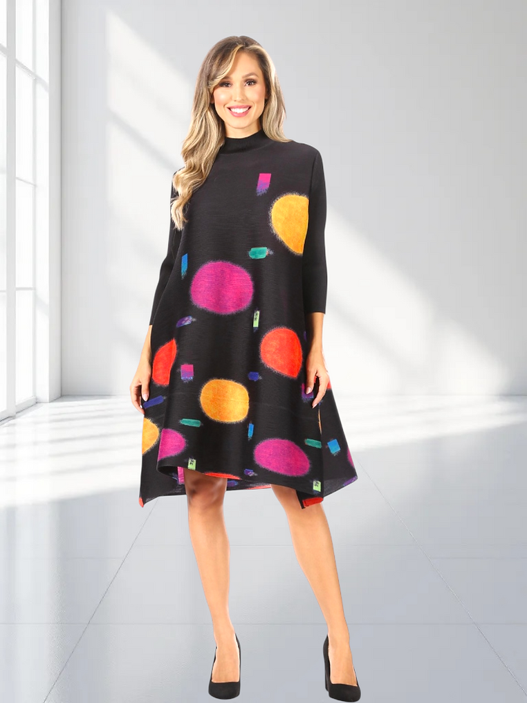 Woman wearing a black dress with colorful polka dots in a bright room.