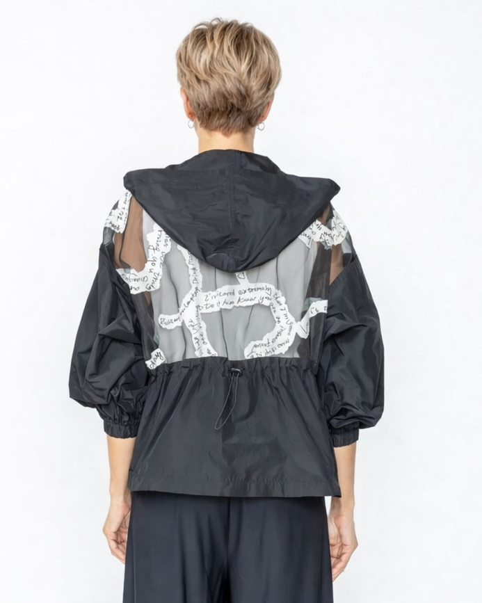 Person wearing a black jacket with sheer panels and wide-leg pants on a white background