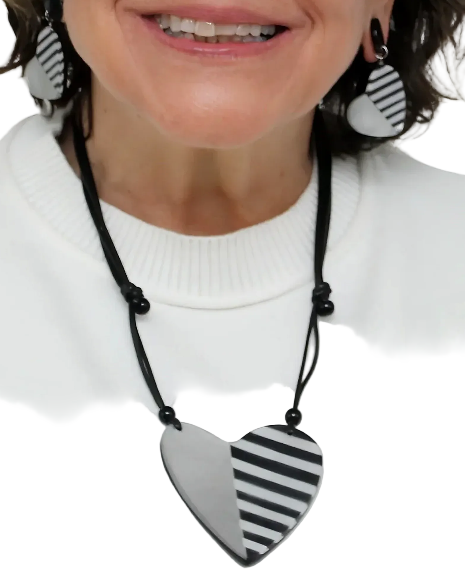 Person wearing a necklace with a heart-shaped black and white striped pendant on a plain background