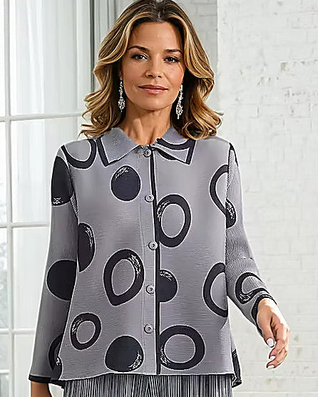 Woman wearing a gray patterned shirt and pants standing in a room with a white brick wall.