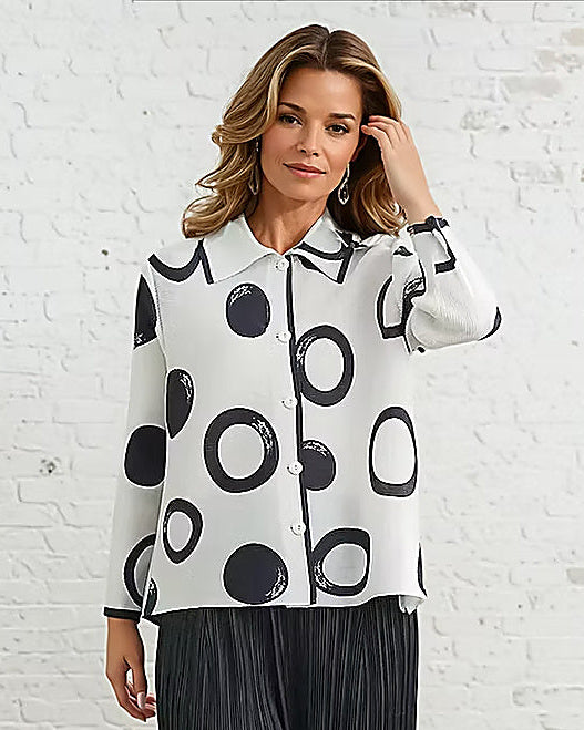 Woman wearing a black and white polka dot shirt and black pants in a room with a white brick wall.